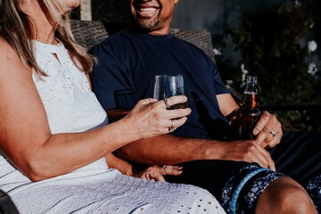 A couple enjoying drinks outdoors. They are seated, holding beverages, and smiling. Relaxed atmosphere with casual clothing and a sunny setting. Couple sitting together, diverse couple.