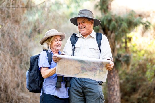 Older couple woman and man hiking and exploring in nature. Couple in hiking outfits holding the map. Outdoor adventure for older adults. Elderly people enjoying outdoors adventure.
