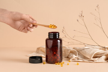 Female hand with bottle of fish oil capsules, napkin and dried flowers on color background
