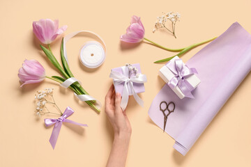 Female hands with gift boxes, flowers and wrapping paper on light yellow background. International Women's Day