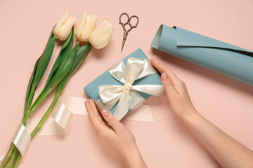 Female hands with gift box, tulips and wrapping paper on beige background. International Women's Day