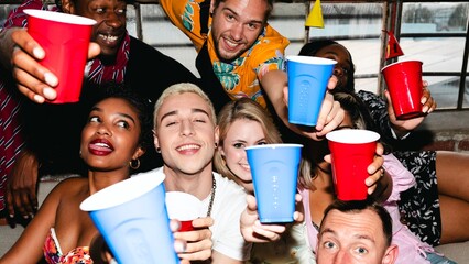 Group of diverse friends celebrating with colorful cups, smiling and enjoying a party. Lively atmosphere with cheerful expressions and festive vibes. Diverse friends drinking at college dorm party.
