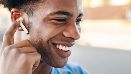 Fototapeta premium Smiling African American man wearing wireless earbuds, enjoying music. Close-up of a happy African American person with earbuds, listening to music. African American man smiling wearing earbuds.