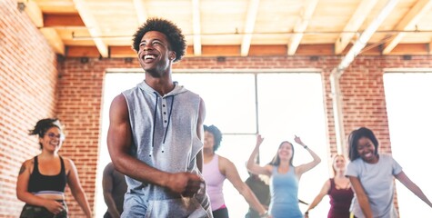 Smiling African American man in a group dance class. The African American man is leading the class. Other participants follow the African American man's moves.