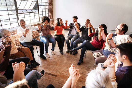 Diverse group in a circle holding hands, showing unity and connection, sharing a moment of togetherness and community. Diverse people sitting in a circle of support from community.