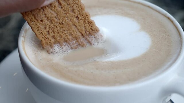 Enjoying a biscuit dipped in creamy coffee at a cozy cafe