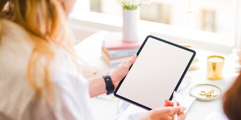 Person holding a blank tablet at a desk. Tablet is blank, ready for notes. Bright workspace with tablet. Tablet focus in a creative setting. Fashion designers working together with tablet.