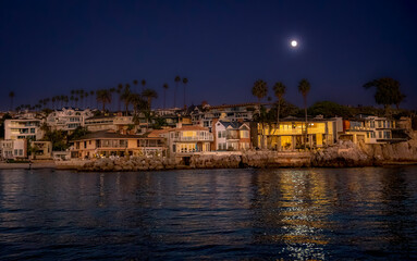 Nightfall at Newport Beach with a strong moonlight above reveals a glow-like surface of reflecting water, beach, beachfront homes and silhouette of Palm Trees 