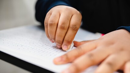 Close-up of a hand erasing answers on a test sheet. The hand is using an eraser on a...