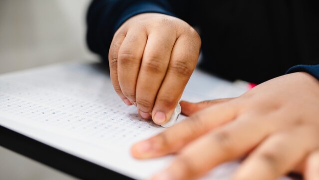 Close-up of a hand erasing answers on a test sheet. The hand is using an eraser on a multiple-choice test. Erasing mistakes on a test paper. Young student erasing answer in exam. Exam in school.