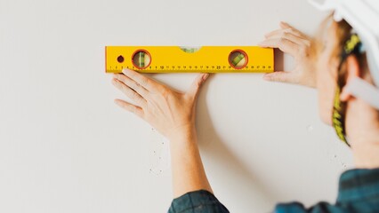 Person using a yellow level tool on a wall. Hands adjusting the level tool. Construction and precision. DIY project with a yellow level tool. Construction in a home.