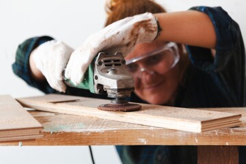 Person using a power tool on wood, wearing gloves and safety goggles. Focused on woodworking, the individual is engaged in a carpentry project. Woodworking and construction work concept.