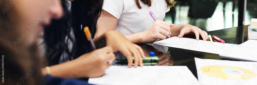 Poster students writing with pens on paper at a desk. focus on hands and writing. diverse group engaged in 