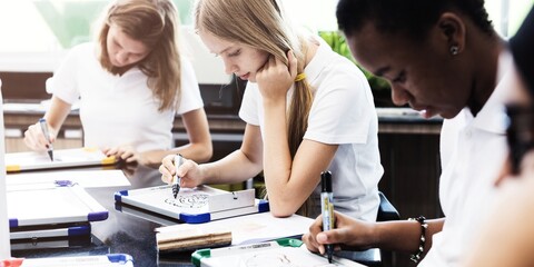 Students focused on drawing in a classroom. Diverse group of young women engaged in art. Concentrated students sketching in an educational setting. Diverse students in classroom, education.