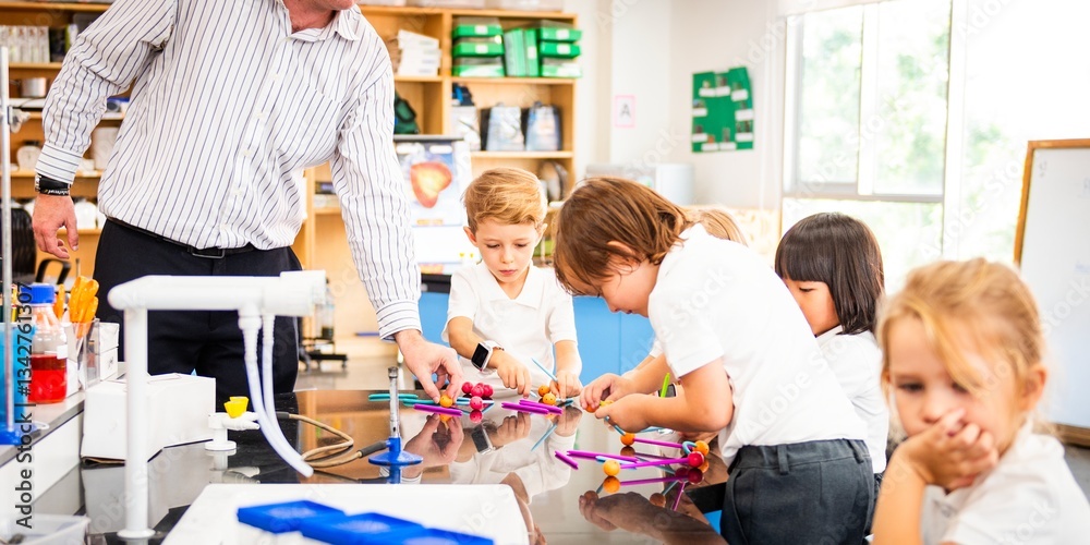 Poster Children in a classroom engaged in a science experiment. Kids learning science with hands-on activities. Teacher guiding students in a science class. Science teacher teaching school kids.