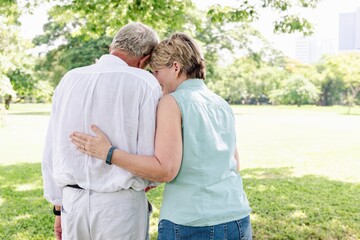 Naklejka premium Elderly couple hug and enjoy sunny day in park. Happy elderly couple share love moment outdoors, surrounded by greenery park nature. Elderly couple enjoy nature, hugging each other, lovely couple