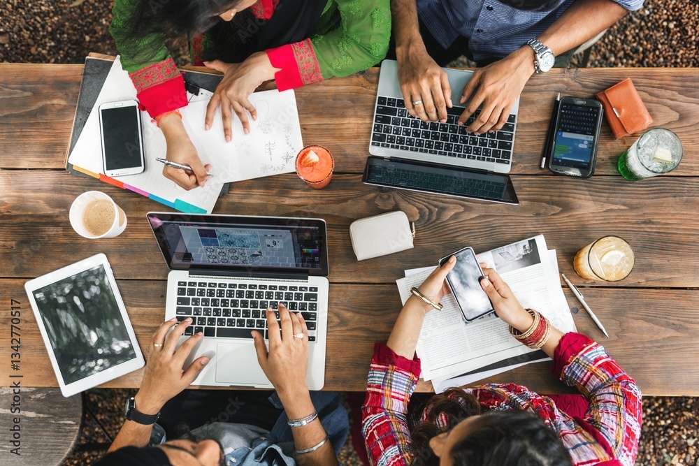 Poster an indian group of friends, collaborate at a wooden table, using laptops and smartphones for a produ