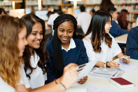 Diverse group of young women studying together. Women using laptops, collaborating, and learning. Female students, diverse ethnicities, engaged in group study. Young women in high school education. - Powered by Adobe