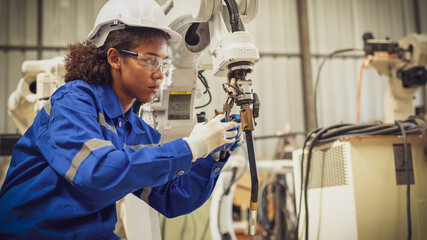 African american engineer woman fixing and testing an Artificial Intelligent welding robotic automatic arm machine in modern technology factory. Automation manufacturing for industry 4.0 Technology. 