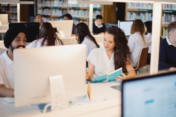 Students studying in a library, with computers and books. Diverse group of students, including an...