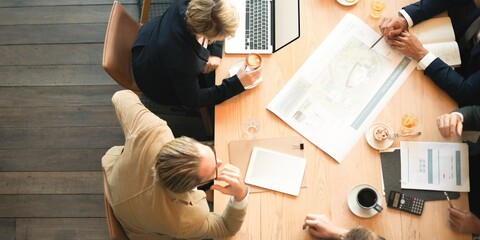 Top view of a diverse group in a business meeting. Professionals discuss plans, laptops open,...