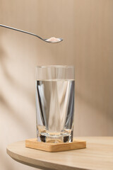 A spoon of Himalayan salt is being added to a glass of drinking water.