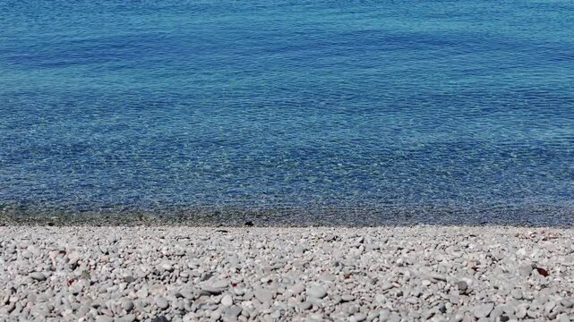 A static shot of a pristine tropical pebble shore at Looc in Surigao City, Philippines, featuring calm, crystal clear waters under sunny blue skies, travel adventure and versatile background b-roll.