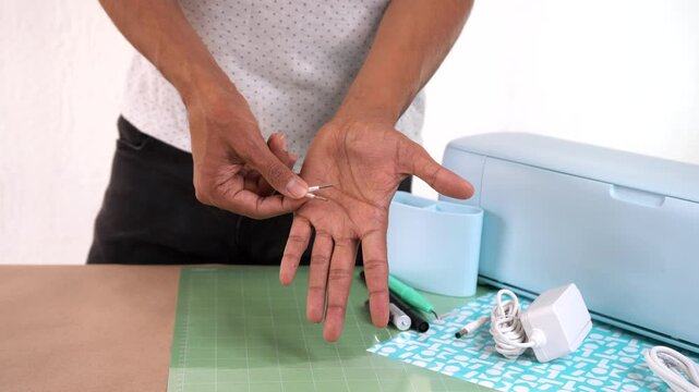 Person holds cutting plotter blade in hands, surrounded by craft tools and workspace