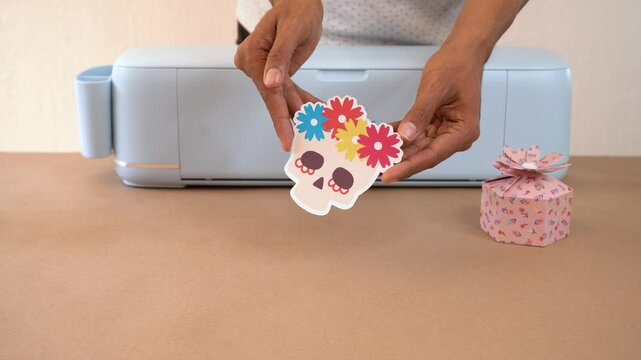 Person displaying colorful paper craft designs, including decorated skull and gift box