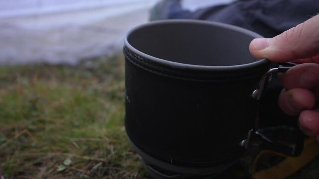 Close-up shot of water being poured into a camping pot inside a tent with grass covered ground.
