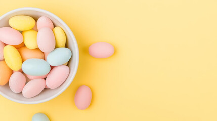 Obraz premium Colorful candy eggs in bowl on bright yellow background create cheerful atmosphere
