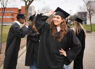 Group of cheerful graduates wearing black gowns celebrating their graduation on a university campus