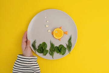Creative culinary concept - a photo of a fish-shaped orange on a plate made from fresh herbs and vegetables