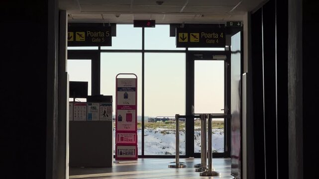 Suceava, Romania - February 19, 2025: A view of the departure gates at Suceava Airport. Signs for Gate 4 and Gate 5 are visible, baggage measurement stand and glass doors leading to the snowy runway.