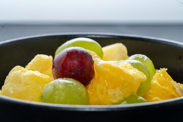 fresh fruit salad. colorful large pieces of grape, orange, pineapple in black bowl, head on, close up, copy space