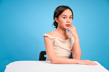 Asian woman sitting at a table with her face resting on one hand, gazing forward with a soft...
