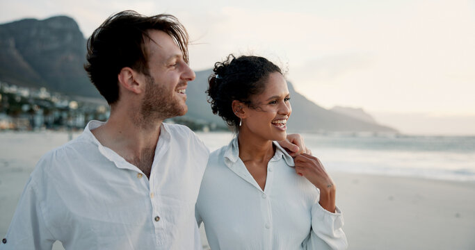 Holiday, travel and interracial couple embrace at beach for love, care or holding hands for relationship. Ocean, happy man and woman outdoor for vacation, laugh or romantic date with view of space