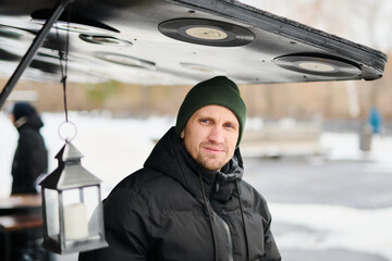 Portrait of young Caucasian man enjoying winter walk in park wearing jacket and warm hat.