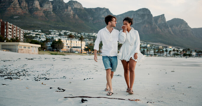 Walking, holding hands and couple kiss at beach for love, care and interracial relationship. Seashore, happy man and woman outdoor for summer holiday, travel or romantic date with partner for support