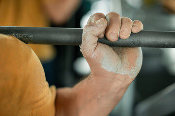 Close-up of a strong hand gripping a barbell with chalk in the gym
