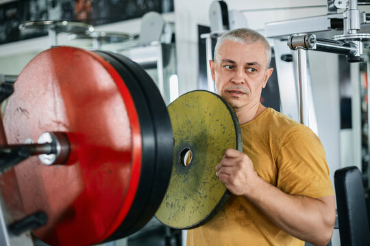 Bald muscular man preparing weight plates for a barbell in the gym