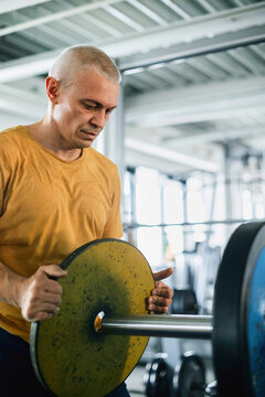 Senior Man Loading Weight Plates onto a Barbell in a Gym