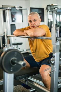 Fit mature man calmly resting on barbell bench in modern gym