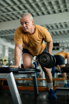 Middle-aged man performing one-arm dumbbell row in a gym