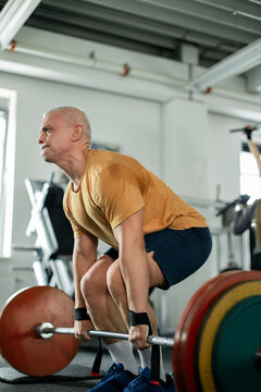 Senior man lifting a heavy barbell with determination in the gym