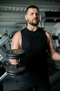 Man in a sleeveless hoodie working out with dumbbells in a gym