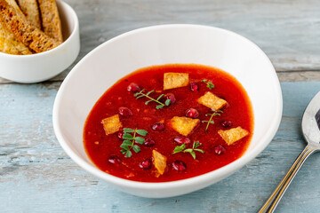 Red soup with pomegranate seeds, croutons, and fresh herbs in a bowl