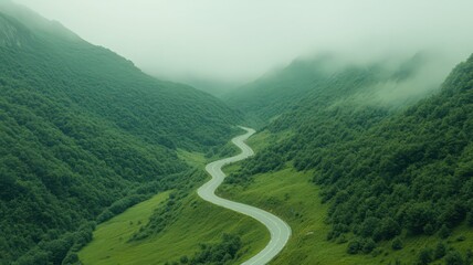 Fototapeta premium Aerial View of Winding Road Through Misty Green Mountain Valley