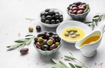 Bowls of various olives with olive oil and olive branches on marble table