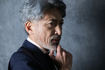 顎に手を当て考えるダンディなグレイヘアの男性　経営者や社長など真剣に考えるイメージの横顔